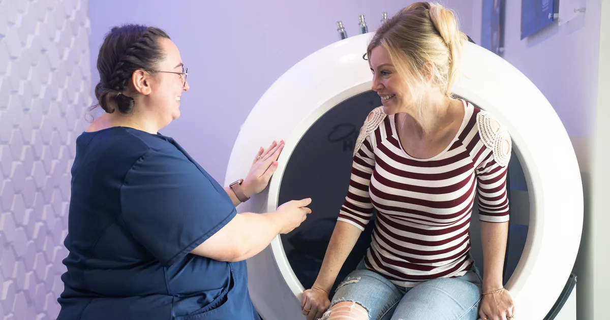 Client sitting in the OxyHealth Fortius 420 hard-shell hyperbaric chamber with a provider at iCRYO South Jordan, UT